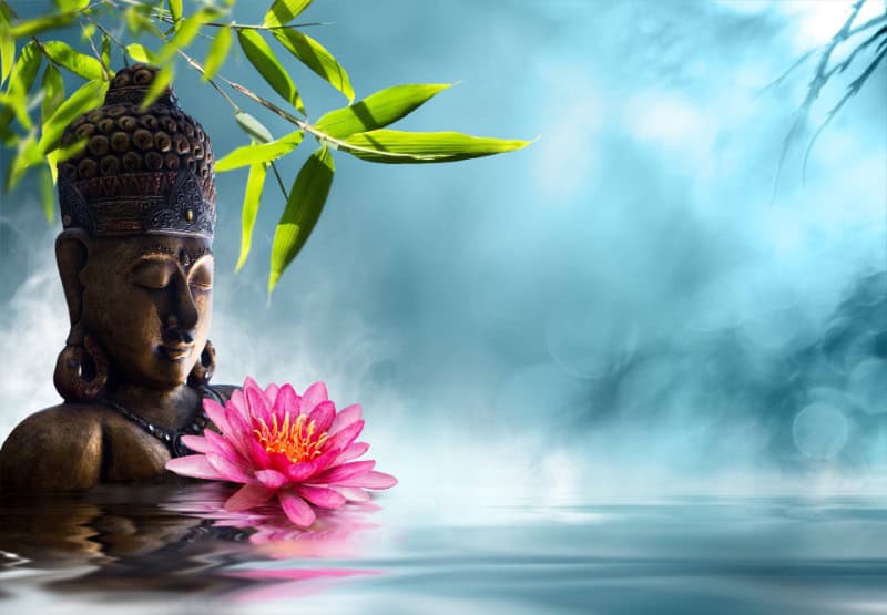 Buddhakopf mit Lotusblume vor einer nebligen Wasserlandschaft.