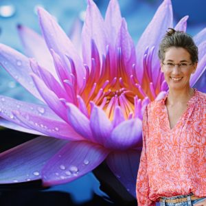Claudia Drescher steht vor einer geöffneten Lotusblume mit Tautropfen im Wasser.